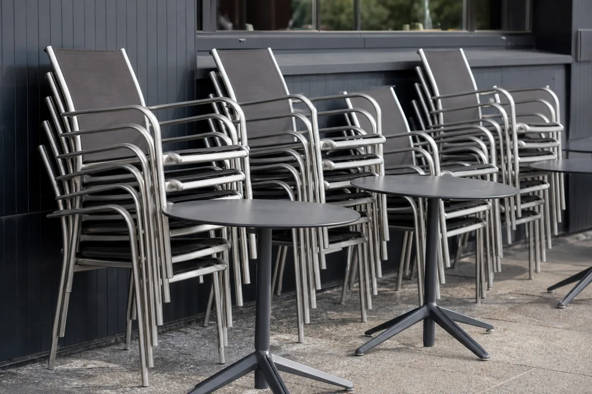 Chaises et tables en aluminium empilées sur une terrasse de restaurant prête pour le service
